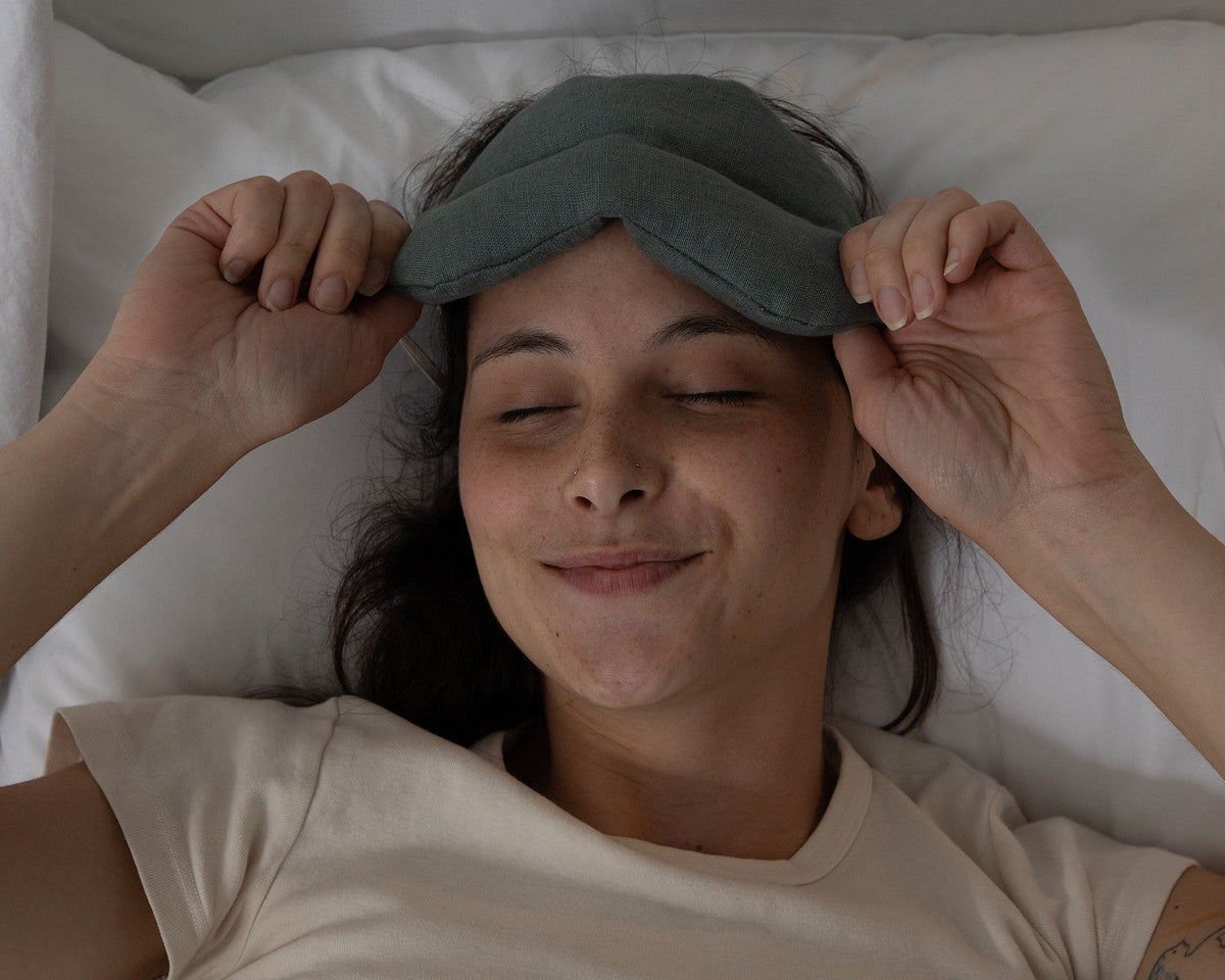 Woman wearing a weighted sleep mask in bed, smiling.