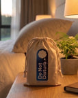 Linen & Wisewool™ sleep mask in its cotton drawstring travel pouch on a bedside table